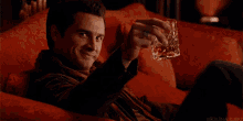 a man sits on a red couch holding a glass of whiskey