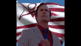 a man in a suit and tie stands in front of a flag