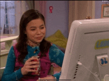 a girl is holding a can of soda and looking at a computer screen
