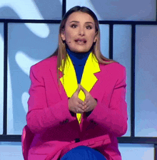 a woman in a pink jacket and blue pants is sitting on a chair