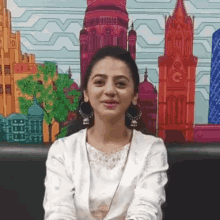 a woman in a white shirt is smiling in front of a painting of a city