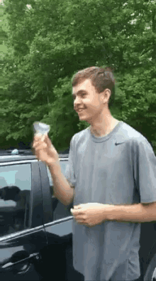a young man in a grey nike shirt is standing in front of a black car