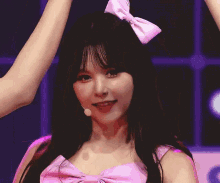 a girl with a pink bow on her head making a heart with her hands