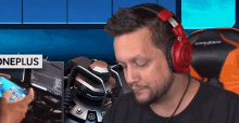 a man wearing headphones is sitting in front of a computer and holding a cell phone .