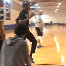 a man wearing an adidas hat stands on a basketball court with other people