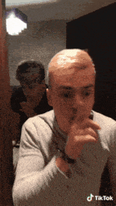 a man covering his mouth with his hand and another man behind him with a tiktok sticker