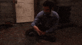 a man in a blue shirt is sitting in front of a door making a funny face