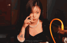 a woman wearing a pearl necklace and a tattoo on her arm is holding something in her hand