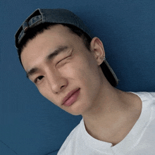 a man wearing a baseball cap and a white shirt winks at the camera