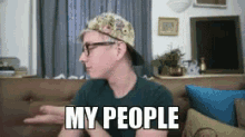 a man wearing a hat and glasses is sitting on a couch with the words my people written on his face .