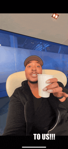 a man sitting in a chair holding a cup that says " to us " on it