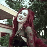a woman with red hair and white paint on her face is wearing a black dress .