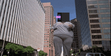 a giant person with a cell phone on their head stands in front of tall buildings