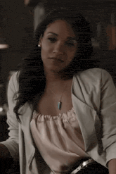 a woman is sitting at a table wearing a white jacket and a pink shirt .