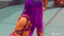 a woman with purple hair is kneeling on the floor in a wrestling match .