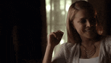 a woman wearing a white shirt and a gold necklace is smiling