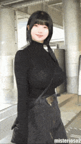 a woman wearing a black turtleneck and a black skirt is standing in front of a sign that says misterioso2