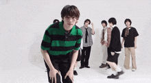 a group of young men are standing in front of a white wall and one of them is wearing a green and black striped shirt