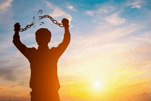a silhouette of a man breaking chains in front of a sunset .