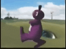 a purple teddy bear is dancing in a field with a windmill in the background .