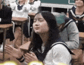 a girl in a sailor uniform is sitting in a classroom with her eyes closed