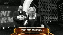 a woman in a black dress is standing next to a man in a suit holding a belt that says timeless