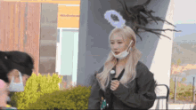 a woman wearing a mask and an angel 's halo stands in front of a building .