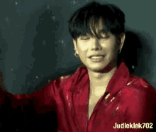a young man wearing a red shirt is standing in front of a black wall .