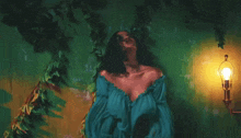 a woman in a blue off the shoulder top is standing in front of a green wall