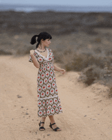 a woman in a floral dress walking down a dirt road