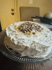 a cake with white frosting and nuts on top is on a glass plate
