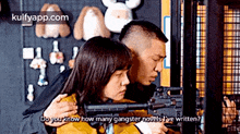 a man and a woman are holding a gun and the man is asking the woman how many gangster novels she 's written .