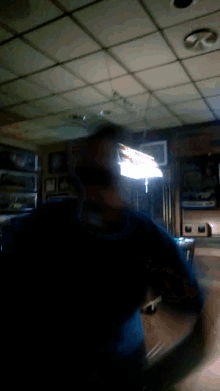 a man in a black shirt is standing in a dark room with a light on the ceiling