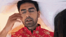 a man in a red shirt is laying on a bed with his eyes closed .