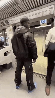 a man in a black jacket and black pants is standing in a train .