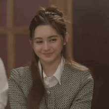 a woman wearing a sweater and a white shirt smiles for the camera