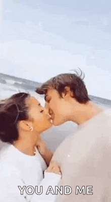 a man and a woman are kissing on the beach and the man is kissing the woman on the cheek .
