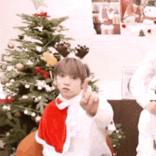 a young man wearing a santa hat is giving the middle finger in front of a christmas tree .