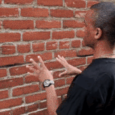 a man wearing a black shirt and a watch is touching a brick wall