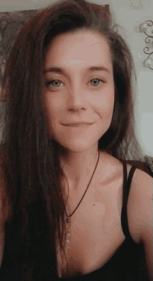 a woman wearing a black tank top and a necklace smiles