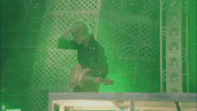 a man playing a guitar in front of a green background with the letter d visible