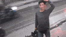 a man in a gray sweater is standing on the sidewalk holding a helmet .