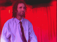 a man in a white shirt and black tie is standing in front of a red curtain