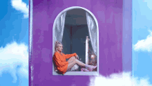 a woman is sitting in a window in a purple building