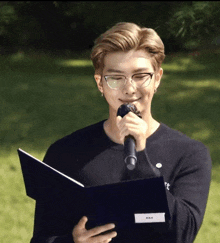 a man wearing glasses holds a microphone and a book