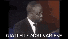 a man in a suit and tie is standing in front of a microphone with the words giati file mou variese written on it .