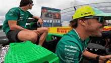 a man wearing a yellow hat with the word aramco on it is sitting in a green race car .