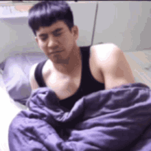a man in a black tank top is wrapped in a purple comforter
