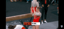 a gymnast is doing a trick on a balance beam while another gymnast looks on .