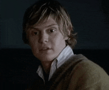 a young man wearing a sweater and a white shirt looks at the camera .